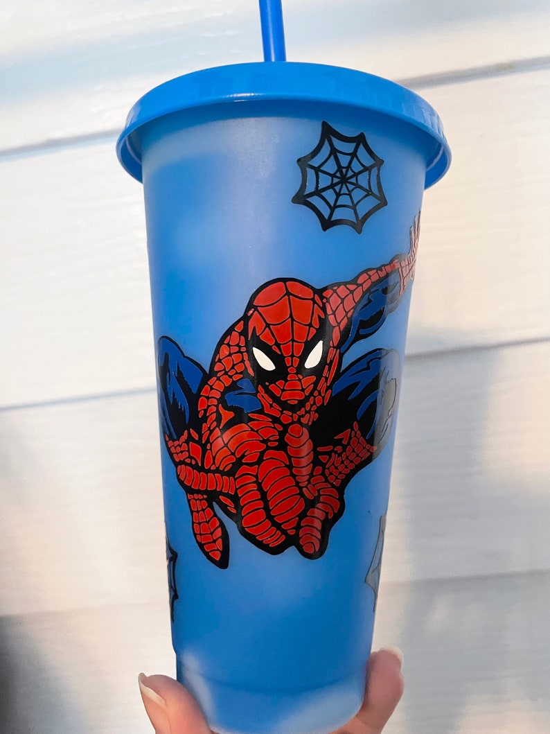 May include: A blue reusable cup with a Spider-Man design. The cup has a black spider web design and a red and blue Spider-Man character.
