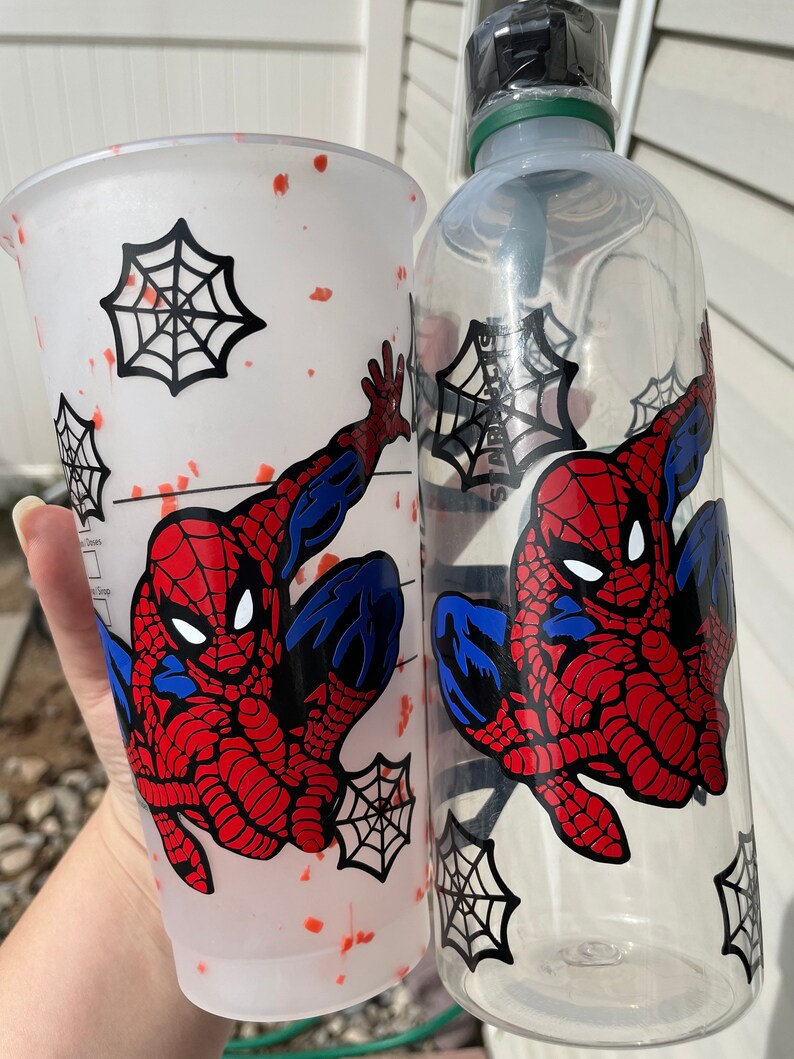 May include: A white tumbler with red splatter paint and a black and white image of Spiderman. A clear water bottle with a black and white image of Spiderman.