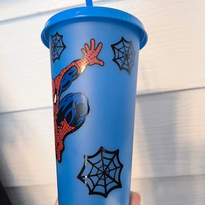 May include: A blue reusable cup with a Spider-Man design and a red straw. The cup has a white swirl design at the bottom and four black spiderwebs.