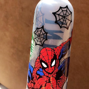 May include: A clear plastic water bottle with a green carrying handle. The bottle has a spider web design and a graphic of Spiderman in a red and blue suit.