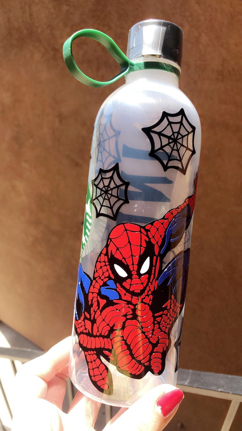May include: A clear plastic water bottle with a green carrying handle. The bottle has a spider web design and a graphic of Spiderman in a red and blue suit.