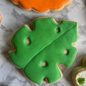 May include: A set of four decorated sugar cookies featuring a lion, a green leaf, and two other cookies. The cookies are decorated with colorful icing and have a whimsical, cartoon-like style.