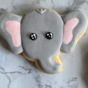 May include: A gray sugar cookie decorated with pink ears and black eyes, shaped like an elephant.