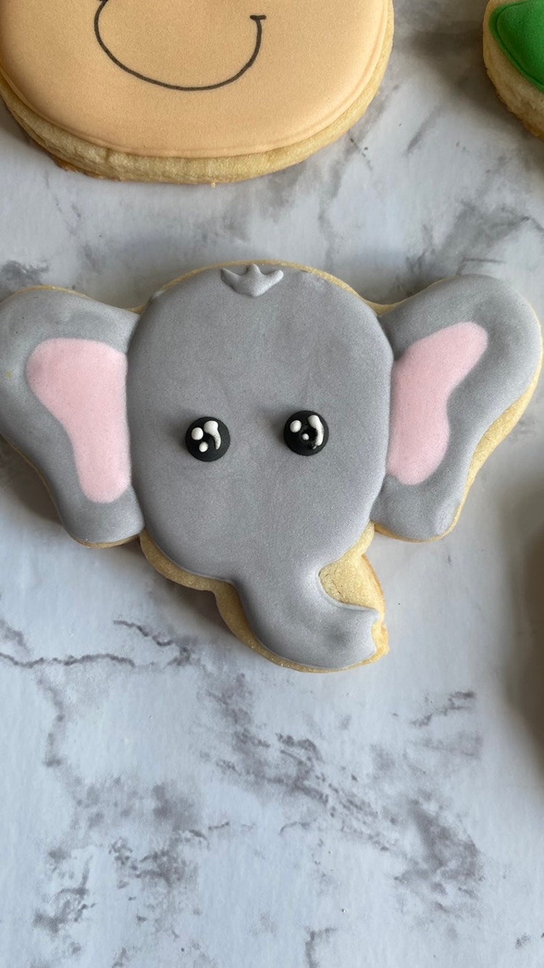 May include: A gray sugar cookie decorated with pink ears and black eyes, shaped like an elephant.