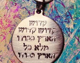 May include: Silver pendant necklace with a round disc featuring Hebrew text. The text reads: "קדוש קדוש קדוש אדוני צבאות מלא כל הארץ כבודו".
