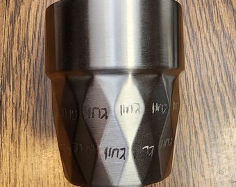 May include: A dark gray metal cup with a diamond pattern and Hebrew text. The cup is made of stainless steel and has a brushed finish.