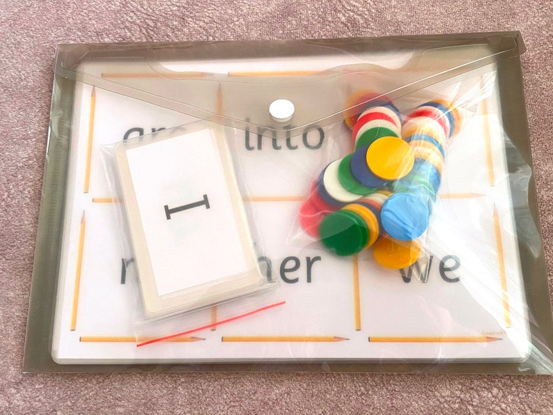 May include: A clear plastic pouch with a white card that says "I" on it. The pouch also contains a variety of colorful counters and two wooden sticks.
