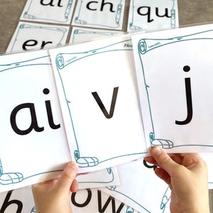 Puede incluir: Un conjunto de tarjetas blancas con bordes de color verde azulado y un diseño de lápiz. Las tarjetas presentan las combinaciones de letras 'ai', 'v' y 'j' en negro.