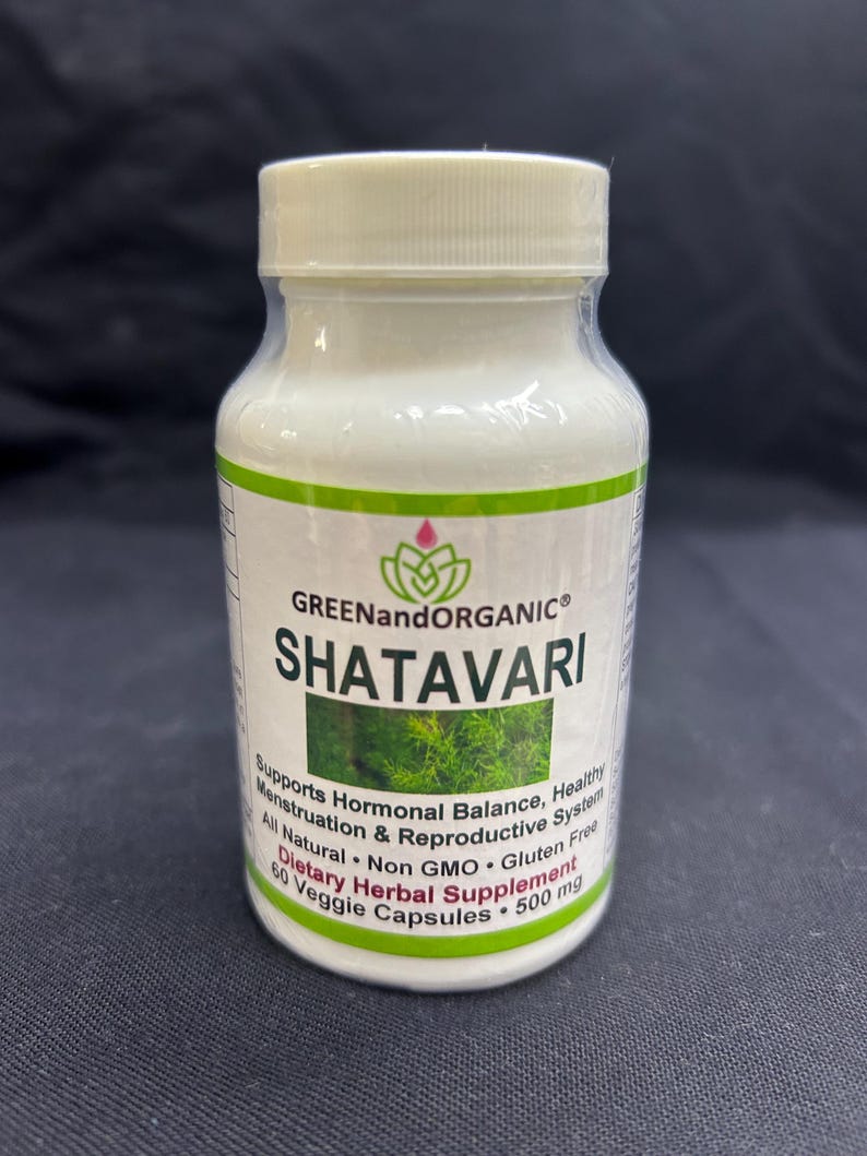 Op de afbeelding: Een witte plastic fles van "SHATAVARI" kruidensupplement met een groen en wit etiket. Het etiket bevat tekst over hormonale balans en reproductieve gezondheid. De fles bevat 60 plantaardige capsules, 500 mg.