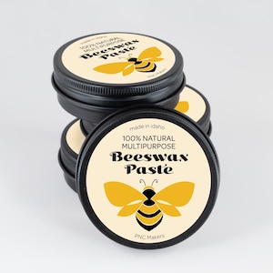 May include: A stack of black tins of beeswax paste. Each tin has a cream-colored label with a yellow bee illustration and the text "100% Natural Multipurpose Beeswax Paste". The text "made in Idaho" is also visible.