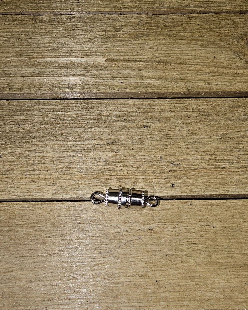 May include: Silver magnetic clasp for necklaces or bracelets. The clasp is made of metal and has a shiny finish.