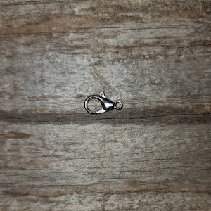 May include: Silver-toned metal lobster clasp, a type of fastener used for jewelry making or attaching to bags or other accessories.