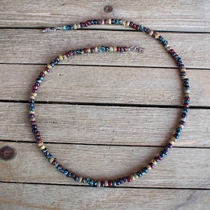May include: A multi-colored beaded necklace with a silver clasp. The beads are a mix of brown, red, blue, and white.