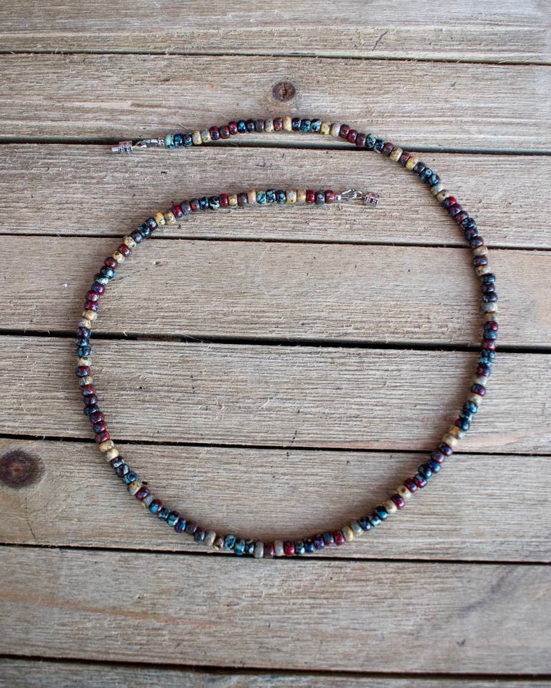 May include: A multi-colored beaded necklace with a silver clasp. The beads are a mix of brown, red, blue, and white.