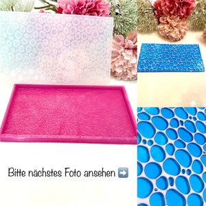 Könnte beinhalten: Eine transparente Silikonform mit einem erhabenen Muster aus kleinen Kreisen. Die Form ist in zwei verschiedenen Farben, weiß und blau, dargestellt. Die Form ist auf einer rosa Oberfläche dargestellt. Der Text "Bitte nächstes Foto ansehen" ist im Bild sichtbar.