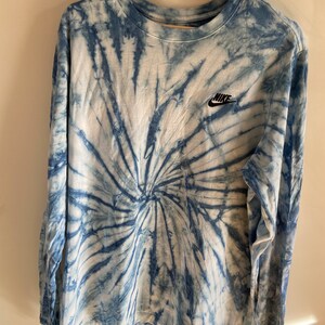 Op de afbeelding: Een blauw en wit tie-dye longsleeve shirt met een zwart Nike-logo op de linkerborst.