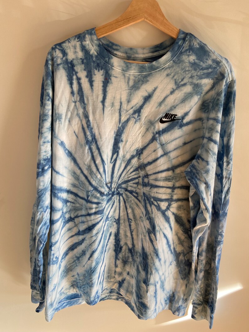 Op de afbeelding: Een blauw en wit tie-dye longsleeve shirt met een zwart Nike-logo op de linkerborst.