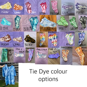 Op de afbeelding: Een verzameling tie-dye sokken in verschillende kleuren, waaronder geel, oranje, roze, blauw, groen, paars en regenboog. De sokken zijn gerangschikt in een rasterpatroon op een lichtpaarse achtergrond. De tekst "Tie-dye kleuropties" staat onder het raster.