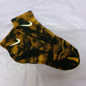 May include: A pair of black and brown tie-dye ankle socks with a white Nike swoosh logo on each sock.