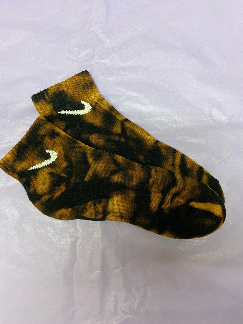 May include: A pair of black and brown tie-dye ankle socks with a white Nike swoosh logo on each sock.