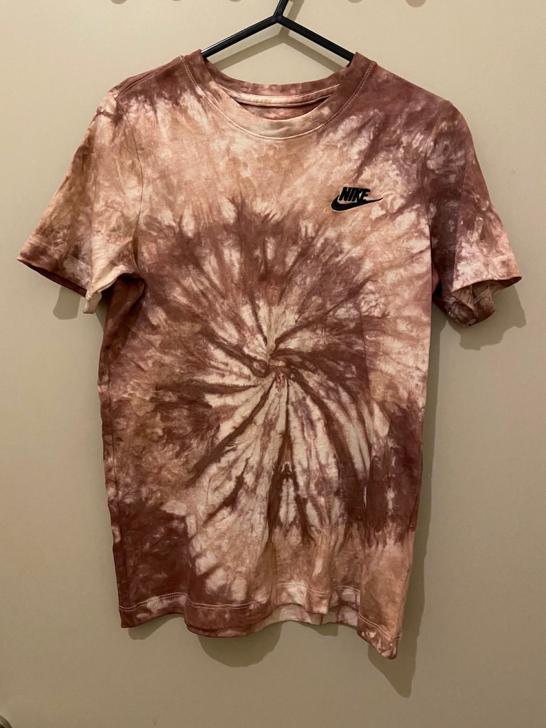 Op de afbeelding: Een bruin en wit tie-dye T-shirt met een zwart Nike-logo op de linkerborst.