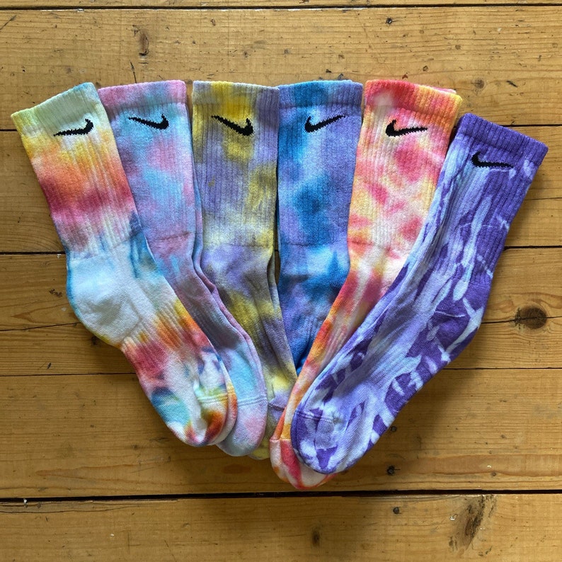 May include: Six pairs of colorful tie-dye socks with a black Nike logo on each sock. The socks are in shades of blue, purple, yellow, and pink.