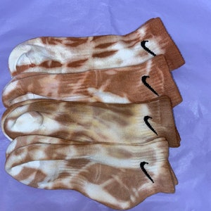 May include: Four pairs of brown and white tie-dye socks with a black Nike swoosh logo on each sock.