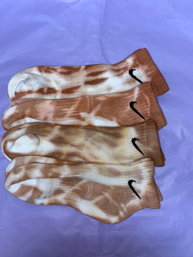 May include: Four pairs of brown and white tie-dye socks with a black Nike swoosh logo on each sock.
