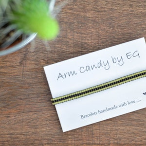 Op de afbeelding: Een witte kaart met de tekst "Arm Candy by EG" en een zwart en groen kralenarmband. De kaart vermeldt ook "Bracelets handmade with love..."