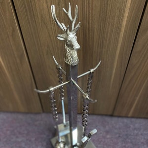 May include: Silver fireplace tool set featuring a deer head design. The set includes a poker, tongs, and a brush.