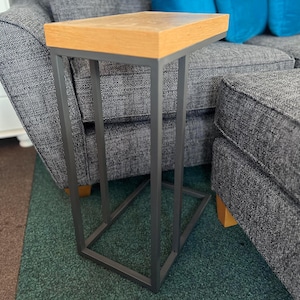 May include: A small wooden table with a black metal frame. The table is sitting in front of a gray couch with blue pillows.