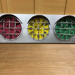 May include: Three round clocks with metal frames and black numbers on a silver background. The clocks are arranged in a row and have different coloured faces: red, yellow, and green.