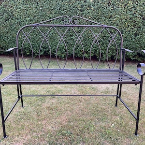 May include: A black wrought iron garden bench with a decorative back and scrolled armrests. The bench has a slatted seat and is set on a grassy lawn. The back of the bench features an ornate design.