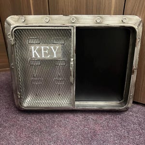 May include: A metal key holder with a wire mesh door and a chalkboard panel. The door has a sign that says "KEY".