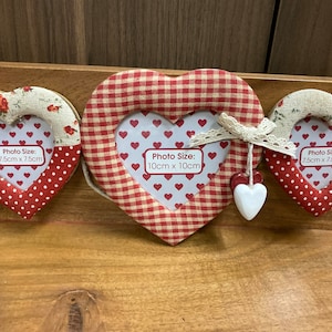 Op de afbeelding: Drie hartvormige fotolijstjes gemaakt van stof met rood-witte ruitjespatronen en rode stippen. De lijstjes zijn in verschillende maten, waarbij het grootste lijstje 10 cm x 10 cm meet.