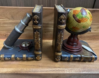 Pode incluir: Um par de porta-livros com um telescópio, uma bússola e um globo. Os porta-livros são feitos de resina e têm um acabamento castanho escuro com detalhes dourados.