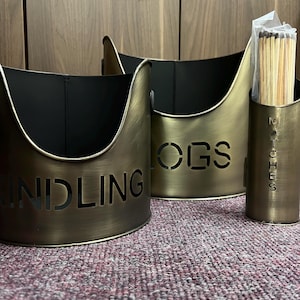 May include: Three gold metal containers for storing kindling, logs, and matches. The containers have cut-out lettering that reads "Kindling", "Logs", and "Matches".