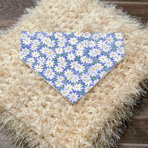 May include: A white, fluffy, crocheted blanket with a blue and white daisy print bandana on top. The bandana has a white border.