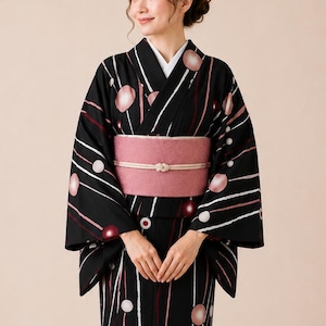 May include: A black kimono featuring a pattern of white and pink vertical lines interspersed with circular motifs in shades of pink, white, and dark red. The garment is secured with a wide, textured dusty pink obi sash tied with a thin white cord.