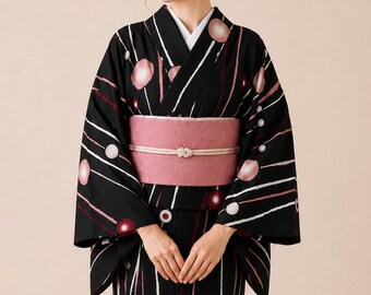 May include: A black kimono featuring a pattern of white and pink vertical lines interspersed with circular motifs in shades of pink, white, and dark red. The garment is secured with a wide, textured dusty pink obi sash tied with a thin white cord.