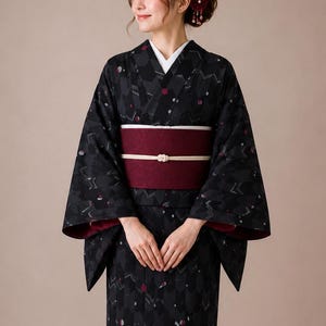 May include: A black kimono featuring a repeating geometric arrow pattern with small red and white circular accents. The garment is cinched at the waist with a wide, solid dark red obi sash, secured by a thin white cord with a central decorative knot.
