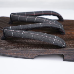 May include: A pair of dark brown wooden geta sandals with black and white checkered fabric straps.