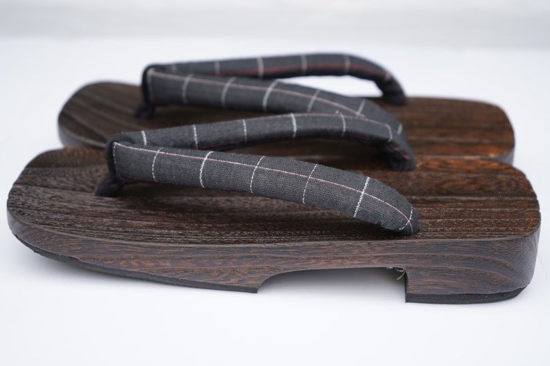 May include: A pair of dark brown wooden geta sandals with black and white checkered fabric straps.