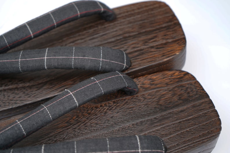 May include: A pair of dark brown wooden geta sandals with black and white checkered fabric straps.