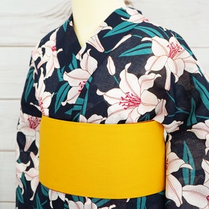 Puede incluir: Un yukata azul marino con un estampado floral de lirios blancos y una faja amarilla. El yukata es una prenda tradicional japonesa que se usa durante los meses de verano.