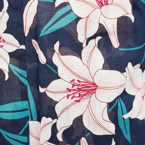 Puede incluir: Una tela azul marino con un patr&oacute;n floral blanco y rosa. Las flores son lirios con centros rosas y p&eacute;talos blancos. El fondo es azul oscuro con una textura sutil.