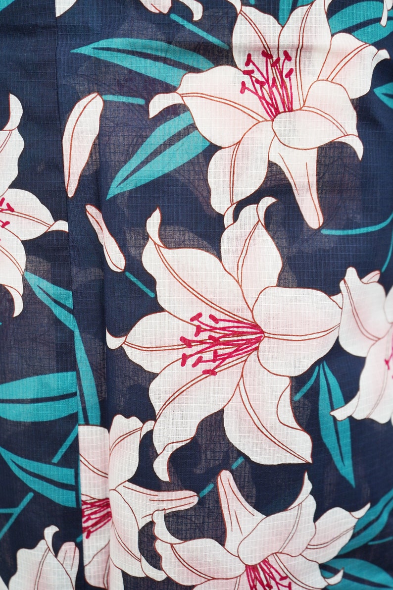 Puede incluir: Una tela azul marino con un patr&oacute;n floral blanco y rosa. Las flores son lirios con centros rosas y p&eacute;talos blancos. El fondo es azul oscuro con una textura sutil.