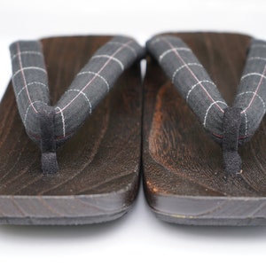 May include: A pair of dark brown wooden geta sandals with black and white checkered fabric straps.