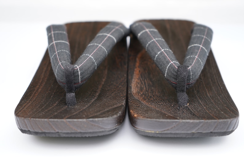 May include: A pair of dark brown wooden geta sandals with black and white checkered fabric straps.
