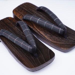 May include: A pair of dark brown wooden geta sandals with black and white checkered fabric straps.